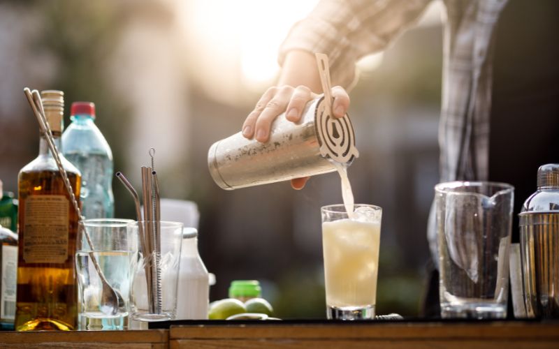 A bartender pouring a cocktail mixture into a glass