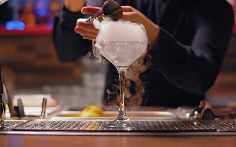 A bartender pouring liquid into a glass with dry ice
