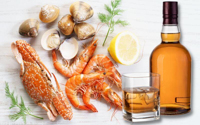 A bottle and glass of whiskey with various seafood on the side
