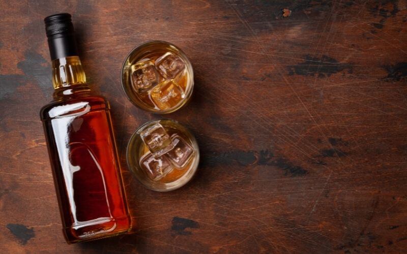 A bottle of brandy beside two glasses of brandy on ice