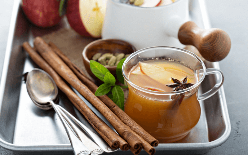 A cup of warm bourbon cider in a tray with spices
