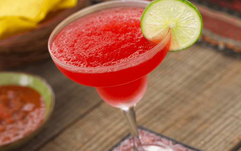 A glass of bulldog strawberry margarita garnished with lime on a woven surface