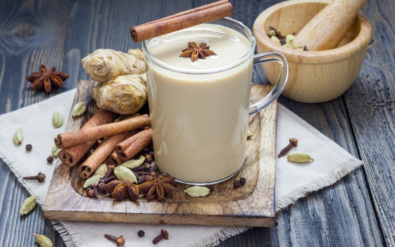 A glass of Vanilla chai Hot toddy in a wooden tray with spices