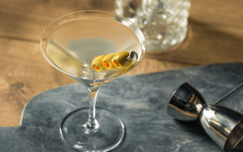 A glass of dirty tequila martini with spiked olives in a marble surface