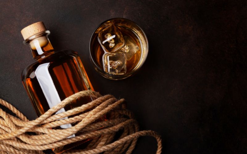A glass of rum and a bottle of rum with rope