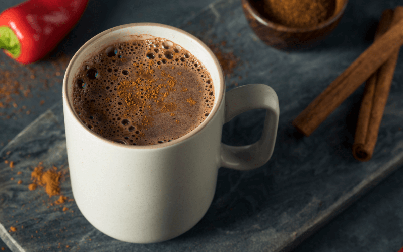 A glass of spiced mexican hot chocolate on a marbled surface