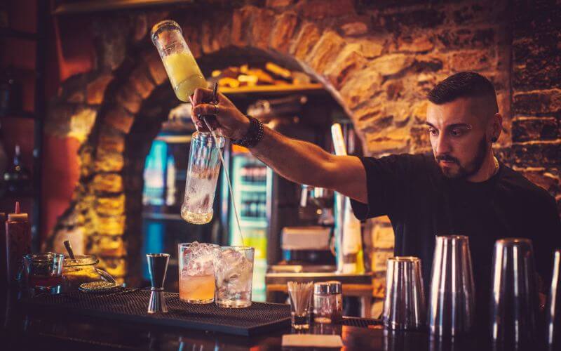 A male bartender free pouring behind the bar