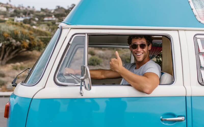 A man doing a thumbs-up while driving a blue van