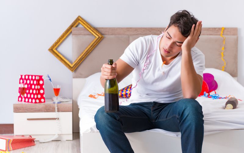 A man suffering from a hangover and holding a bottle of wine