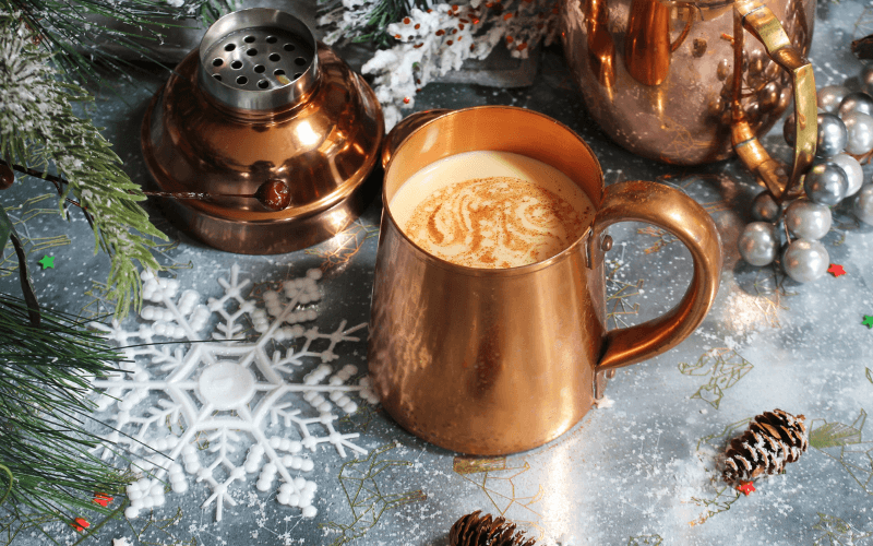 A mug of holiday eggnog cocktail in a Christmas themed background