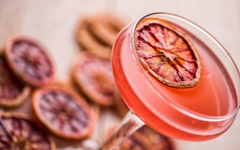 A pink cocktail garnished with dehydrated blood oranges