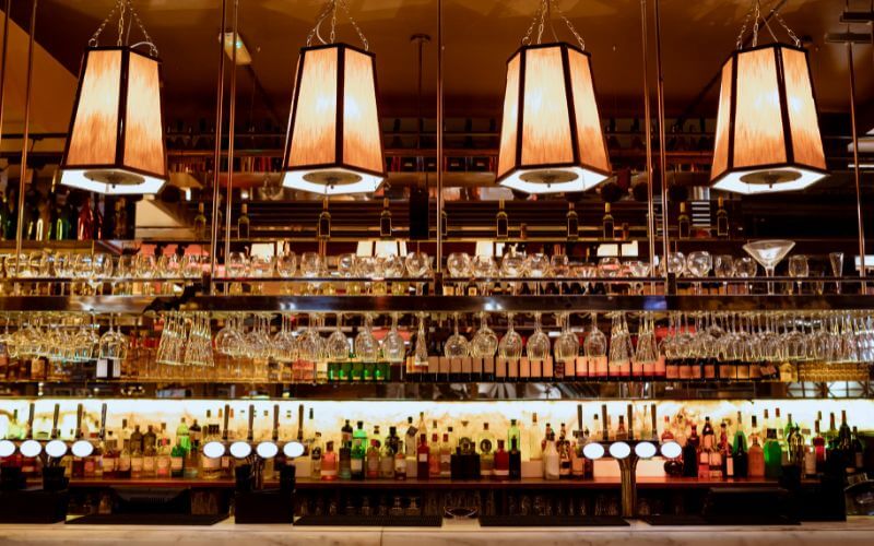 A well-lit bar counter with liquor bottles and wine glasses on the shelves