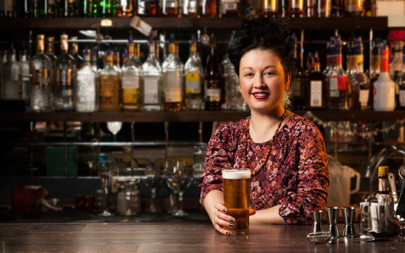 A woman behind the bar holding a glass of beer