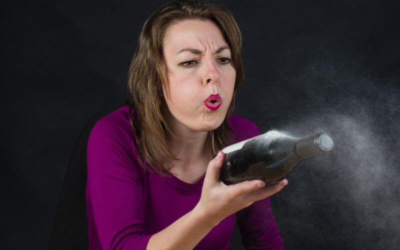 A woman blowing the dust off a bottle of wine