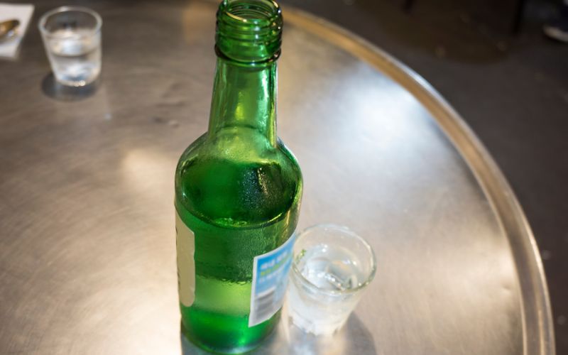 An opened soju bottle with a shot glass