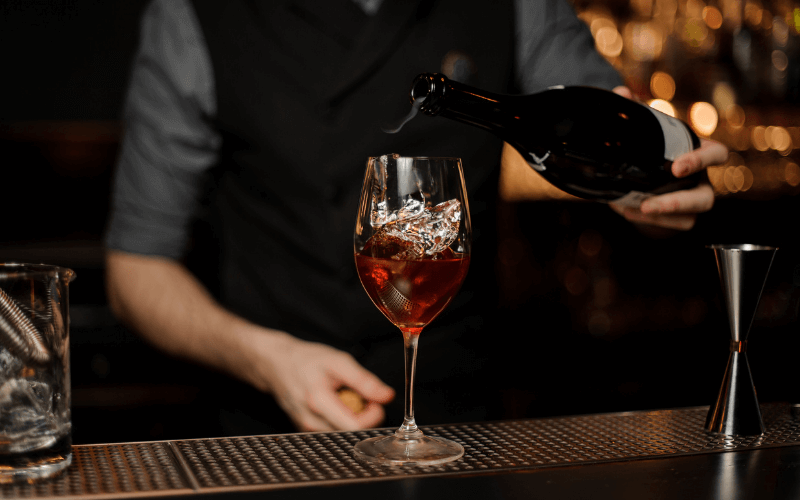 Bartender adds sparkling wine in a cocktail on a bar counter