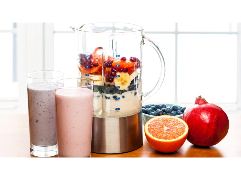 Blender with smoothies and fruits on top of table