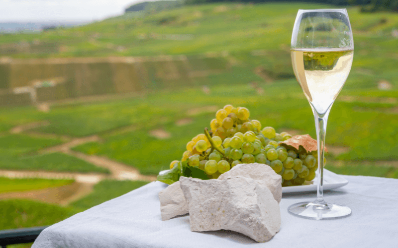 Chalkstone, grapes, and a glass of white wine on a table set against a lush background