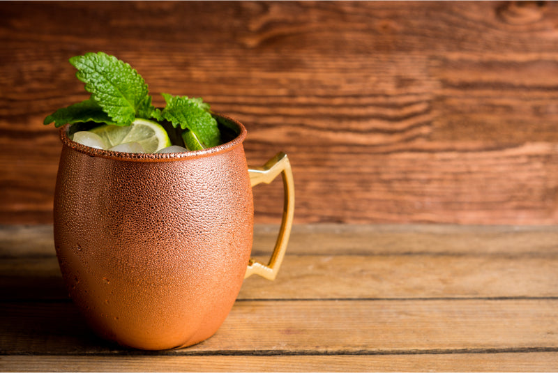 Cold Moscow Mule cocktail in copper mug on rustic background