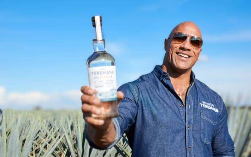 Dwayne Johnson holding his tequila in a plantation - Image by Teremana