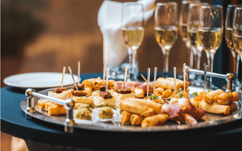 Finger foods on a tray with glasses of Champagne at the back