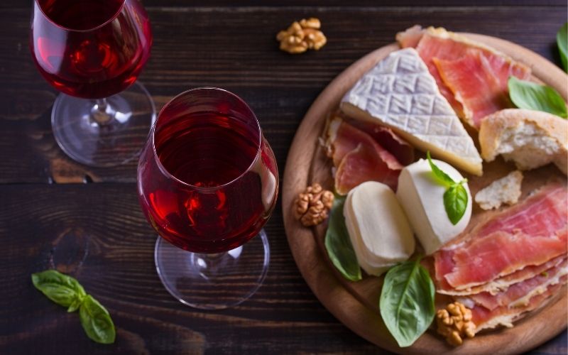 Glasses of wine with cheese, bread, nuts, and prosciutto