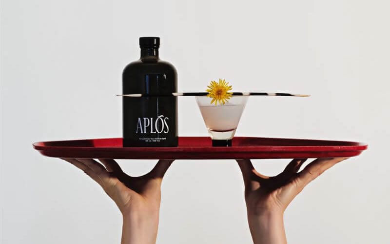 Hands holding a tray of an Aplos bottle and a mocktail
