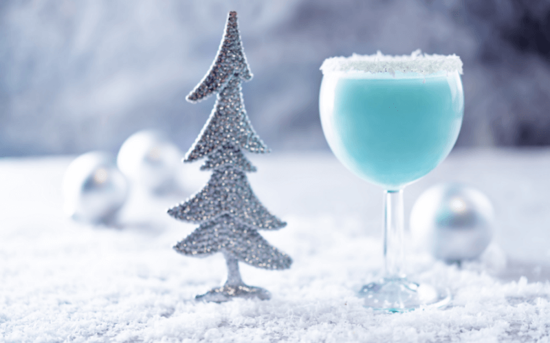 A glass of Jack Frost cocktail in a white-Christmas themed background