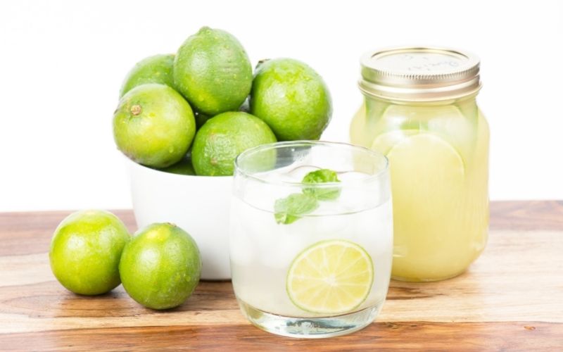 Lime juice in glass and jar with whole limes