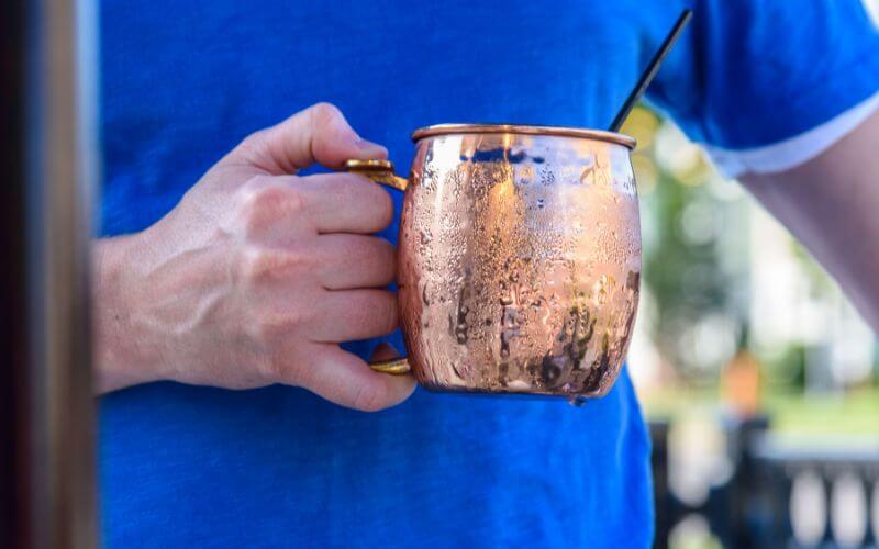 Man holding cold moscow mule drink in copper mug