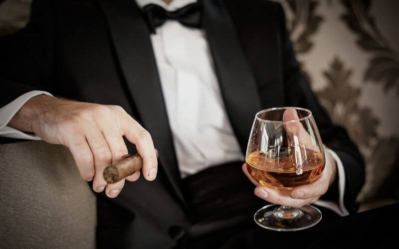 Man in a tuxedo holding a glass of Cognac and a cigar