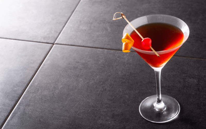 A glass of Manhattan with skewered cherry and orange twist