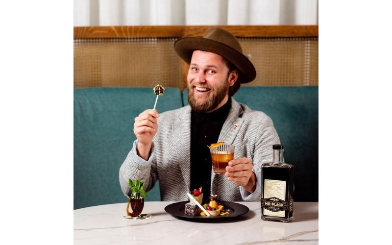 Martin Hudak holding a glass of cocktail and some dessert