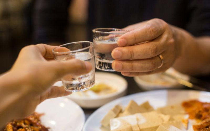 People clinking shot glasses with soju