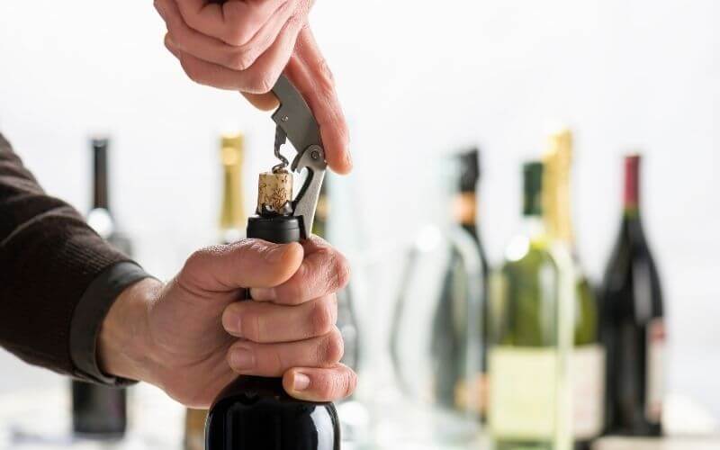 Person opening a wine bottle with a corkscrew