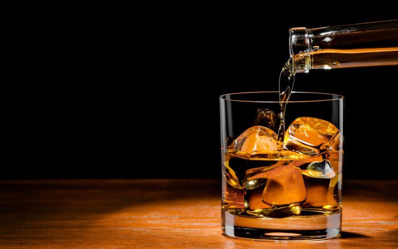 Pouring whiskey into a rocks glass with ice