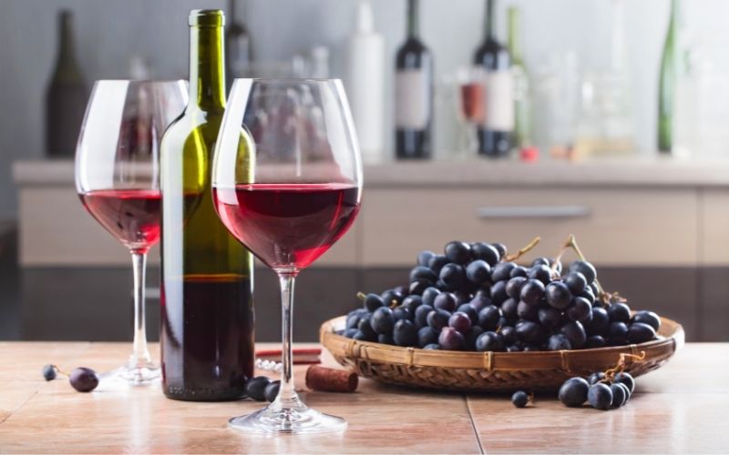 Red wine bottle beside two glasses of wine with red grapes