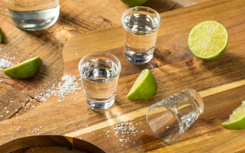 Shots of tequila, lime slices, and salt on a cutting board