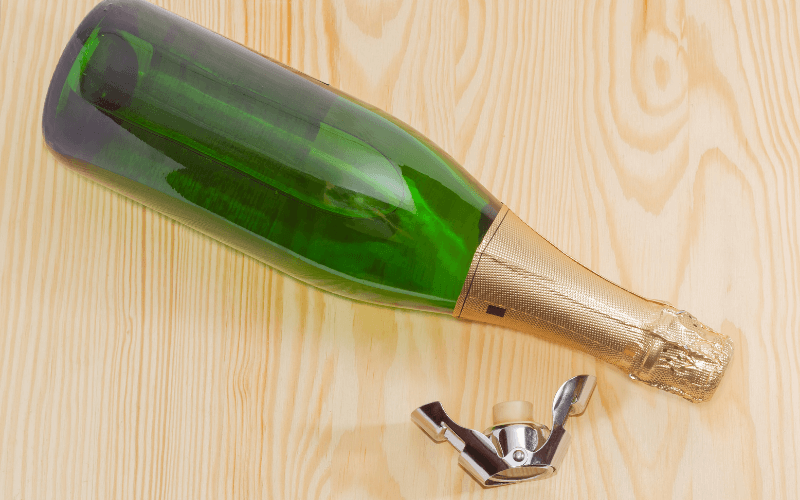 Sparkling wine bottle beside a wine stopper on a wooden surface