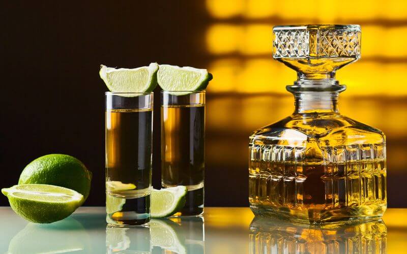 Two shots of tequila with lime beside a bottle