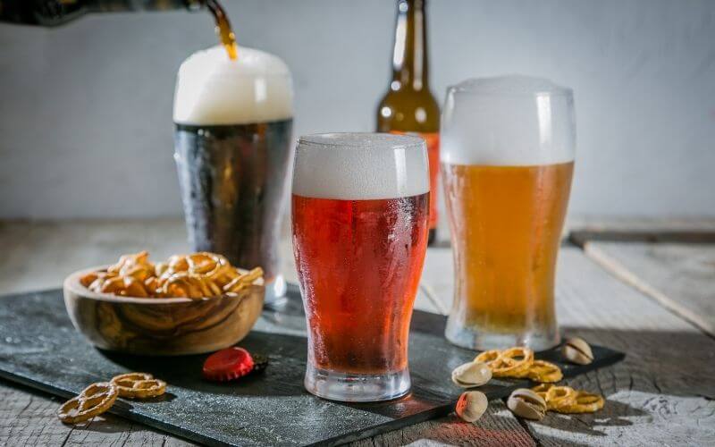 Three glasses of different types of beer and a bowl of pretzel