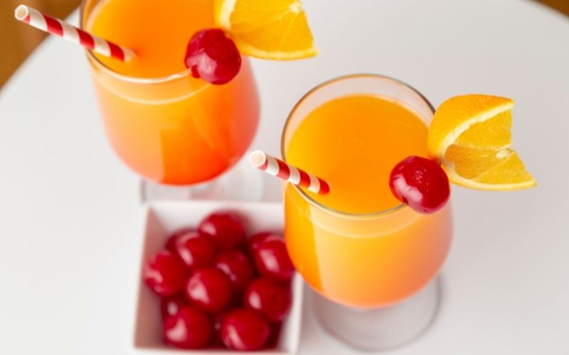 Two glasses of tequila sunrise garnished with cherries