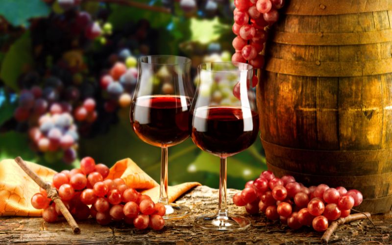 Two glasses of wine beside a barrel and grapes
