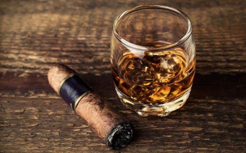 A glass of Sorghum Whiskey beside a cigar