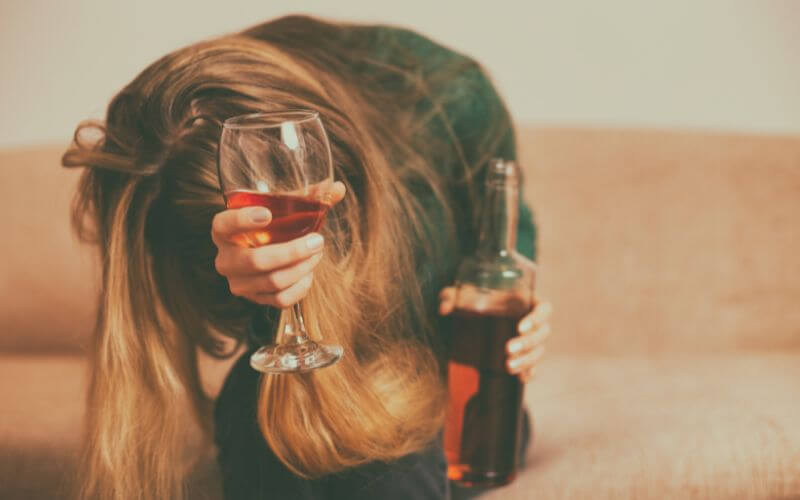 A woman with a bloated stomach holding a glass of alcohol