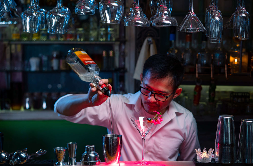 Professional barman pouring blue liquor from bottle into cocktail shake