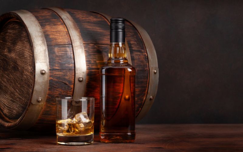 Whiskey bottle beside a rocks glass and an oak barrel