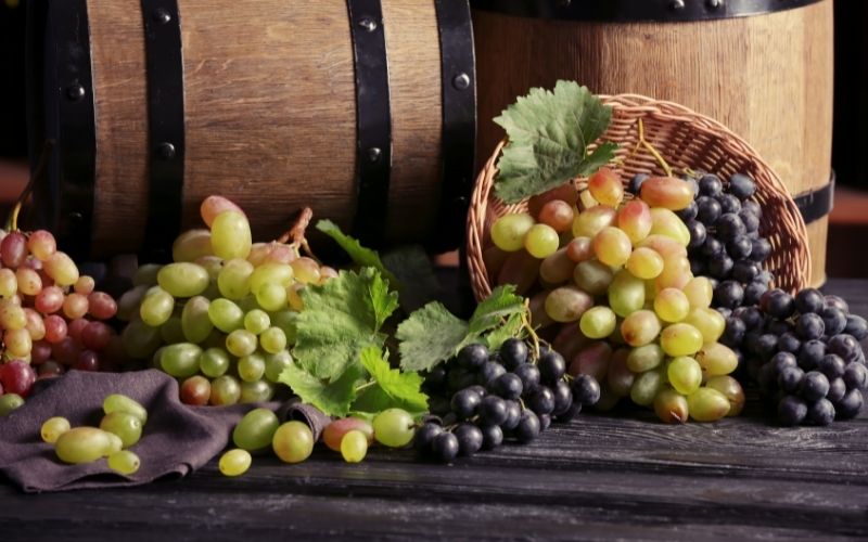 White and black grapes on a table in front of barrels