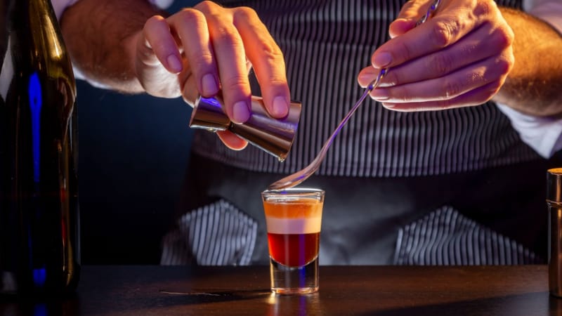 A bartender adding some liquid using the bar spoon and jigger