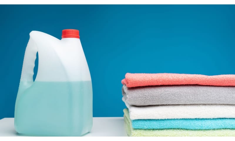 A big bottle of bleach next to a stack of folded towels